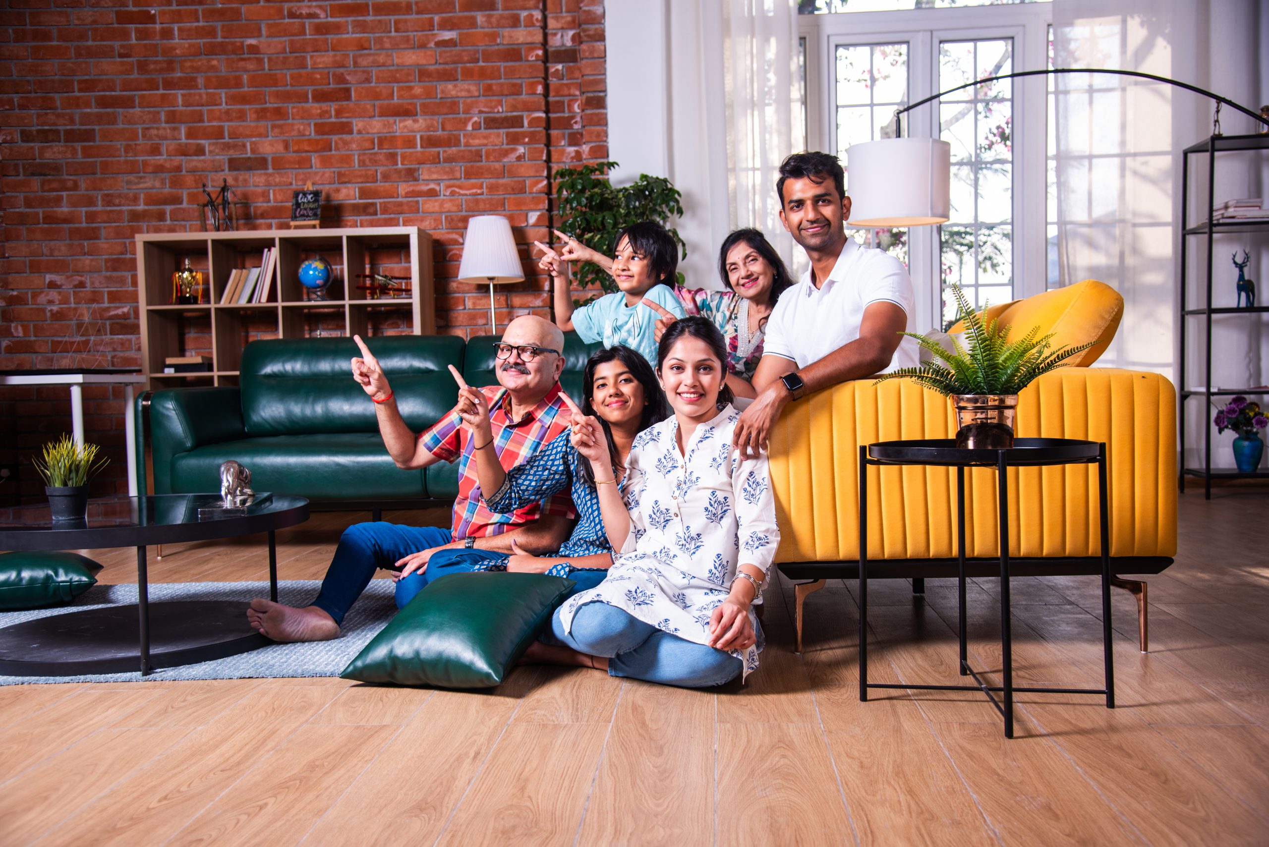 Group photo of Indian asian family of six sitting on sofa looking at camera, presenting or ok sign