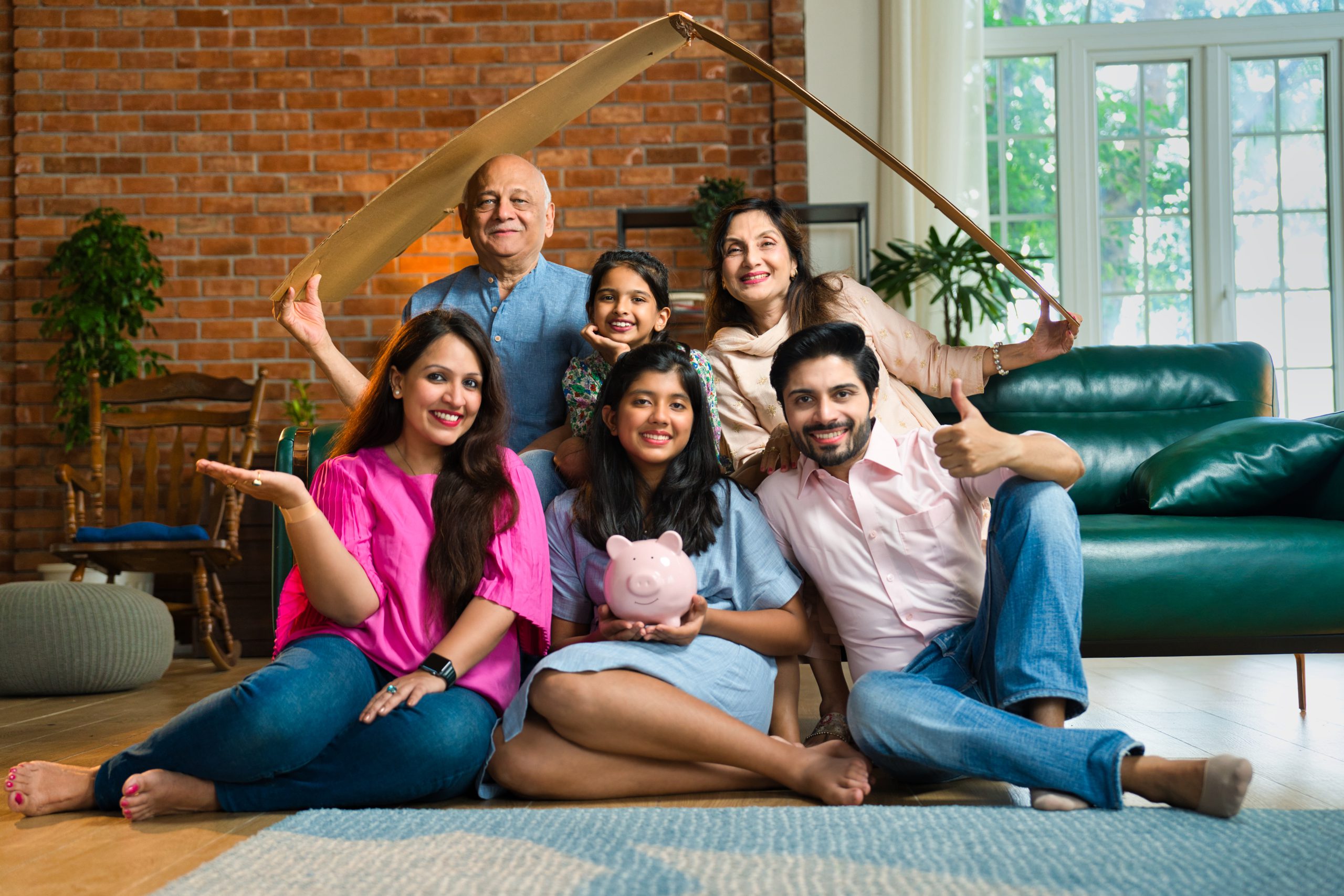 Family of six sitting with cardboard roof and piggy bank, representing real estate and savings calgary equity loans why we're different image of happy family